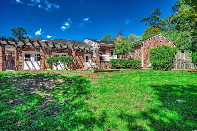 back of house featuring brick siding, a yard, a pergola, and a chimney