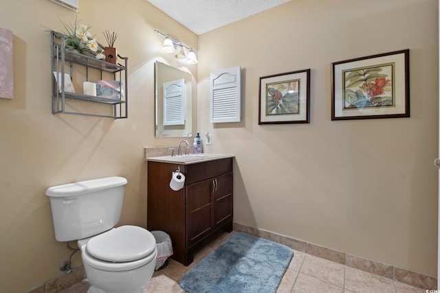 bathroom featuring toilet, vanity, baseboards, tile patterned floors, and a textured ceiling