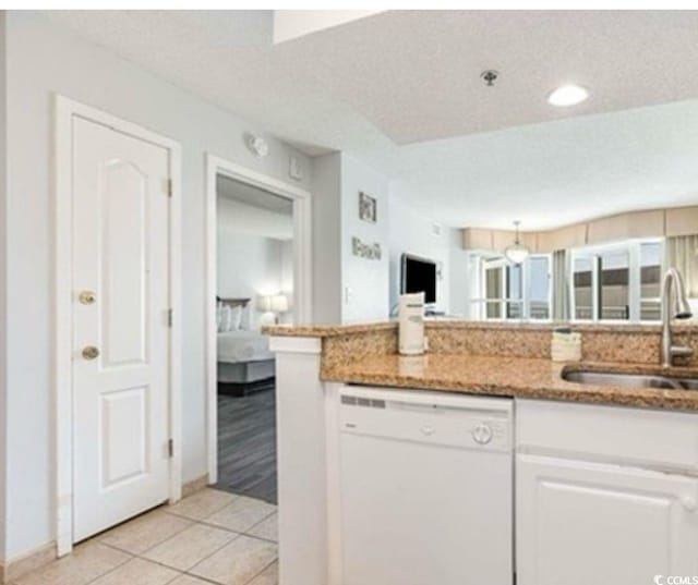 kitchen featuring dishwasher, white cabinetry, light stone counters, a sink, and light tile patterned floors