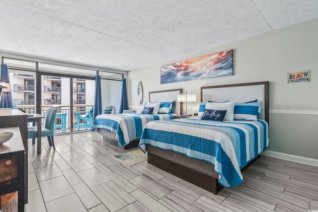 bedroom featuring a textured ceiling, a wall of windows, baseboards, and wood tiled floors