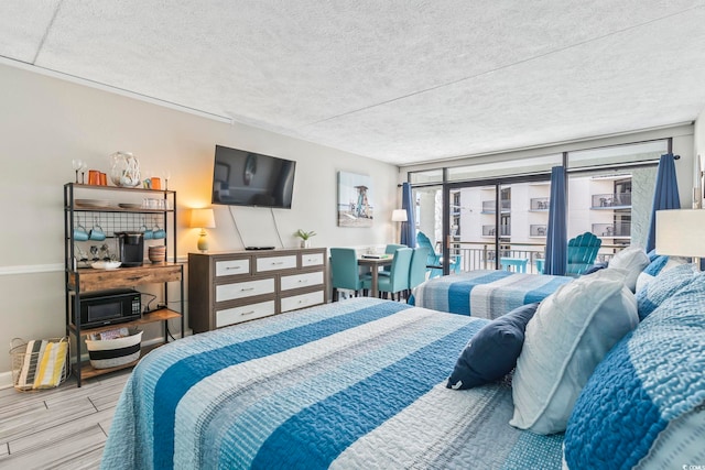 bedroom with a textured ceiling, access to outside, wood finished floors, and baseboards