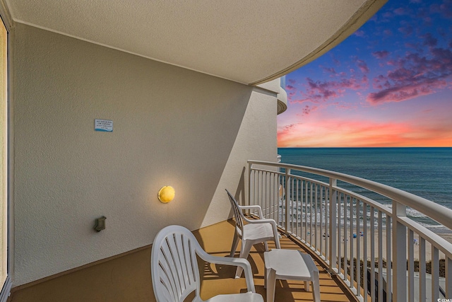 balcony at dusk featuring a water view