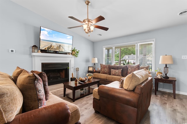 living area featuring a ceiling fan, visible vents, vaulted ceiling, a fireplace with raised hearth, and light wood-style flooring
