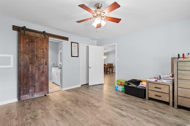 bedroom featuring light wood-style floors, a barn door, baseboards, and connected bathroom