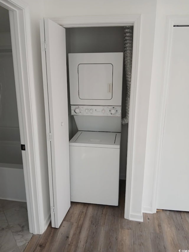 clothes washing area featuring laundry area, stacked washing maching and dryer, and wood finished floors