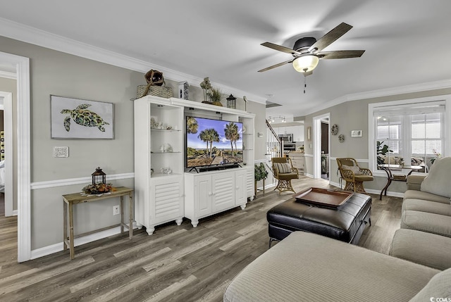 living room featuring wood finished floors, a ceiling fan, crown molding, baseboards, and stairs