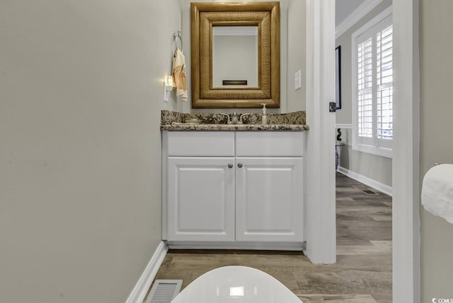 bathroom with baseboards, visible vents, vanity, crown molding, and wood finished floors