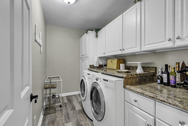 clothes washing area with cabinet space, washer and clothes dryer, wood finished floors, and baseboards