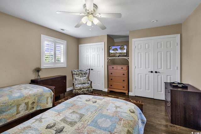 bedroom featuring a ceiling fan, baseboards, dark wood-style flooring, visible vents, and two closets