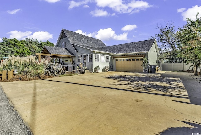 view of front of house with driveway, roof with shingles, a garage, and fence