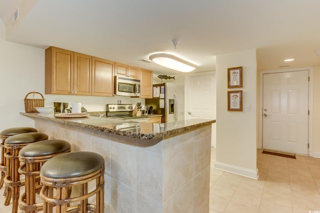 kitchen with stone countertops, a peninsula, a kitchen breakfast bar, and stainless steel appliances