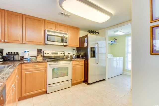 kitchen with visible vents, light tile patterned flooring, washer and dryer, stone counters, and appliances with stainless steel finishes