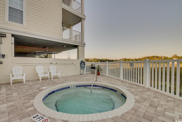 pool at dusk featuring a hot tub, fence, and a patio area