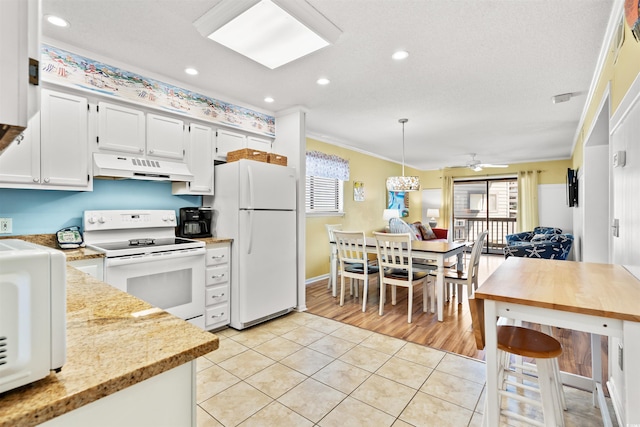 kitchen featuring under cabinet range hood, light tile patterned floors, a wealth of natural light, and white appliances