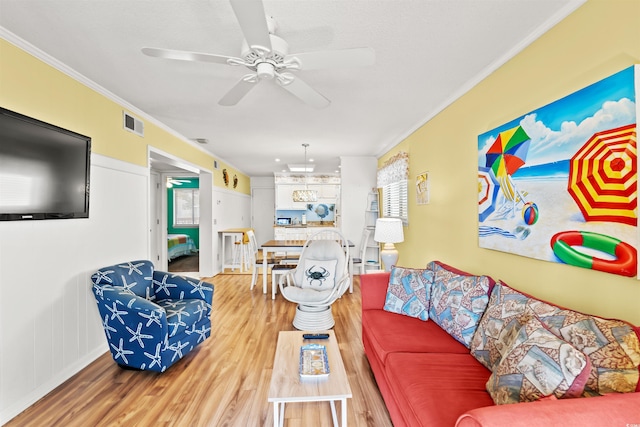 living room with crown molding, light wood finished floors, and ceiling fan