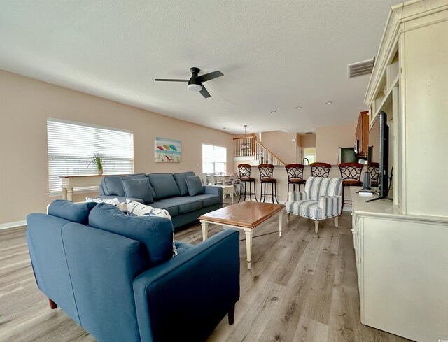 living room featuring light wood-style flooring, a ceiling fan, and baseboards