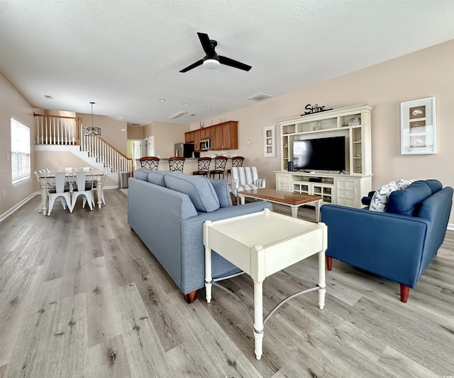 living room featuring light wood-style floors, ceiling fan, stairs, a textured ceiling, and baseboards