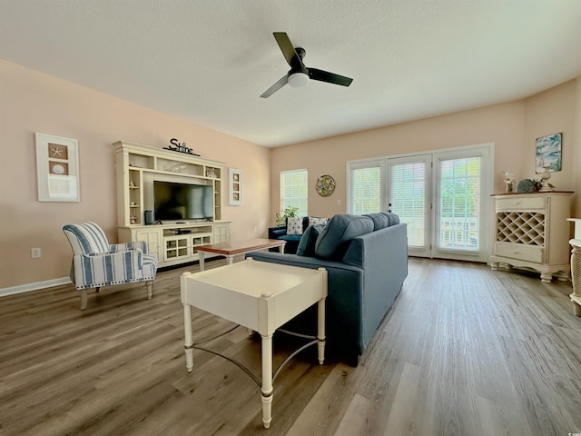 living area with wood finished floors, ceiling fan, a textured ceiling, and baseboards