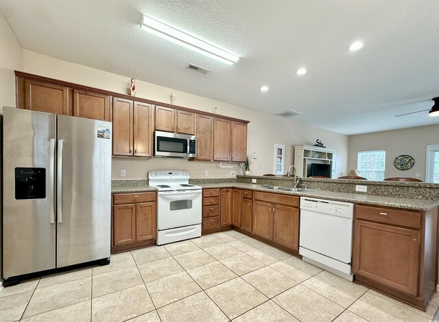 kitchen featuring stainless steel appliances, a sink, a peninsula, brown cabinets, and recessed lighting