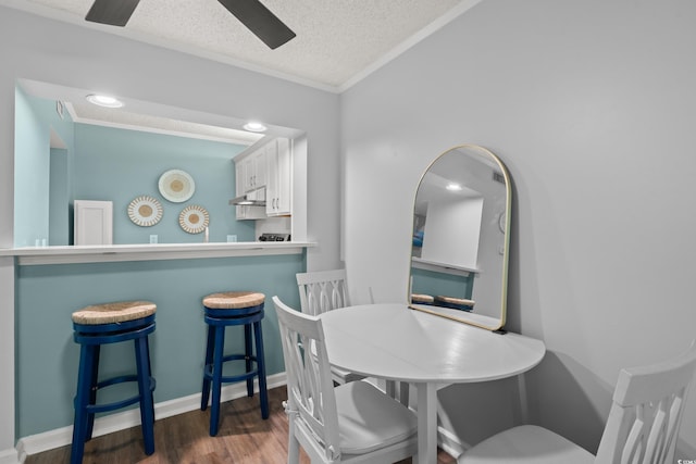 dining room with a ceiling fan, a textured ceiling, wood finished floors, baseboards, and ornamental molding