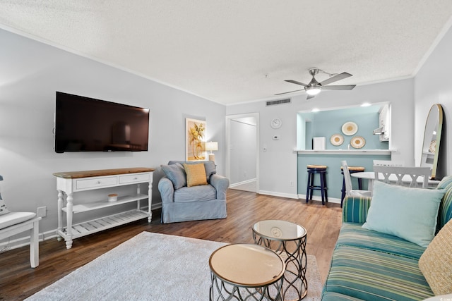 living room featuring crown molding, ceiling fan, a textured ceiling, wood finished floors, and visible vents