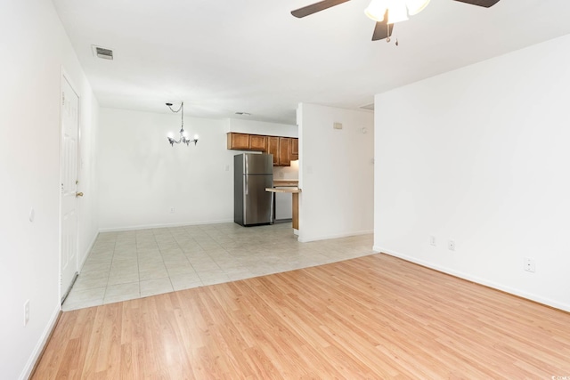 unfurnished living room with baseboards, visible vents, ceiling fan with notable chandelier, and light wood-style floors