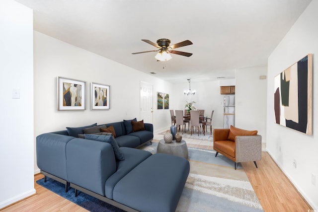 living area featuring baseboards, ceiling fan with notable chandelier, and light wood-style flooring