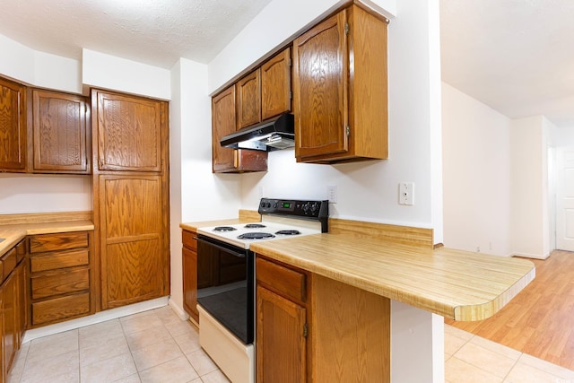 kitchen with electric range oven, under cabinet range hood, light countertops, and brown cabinets