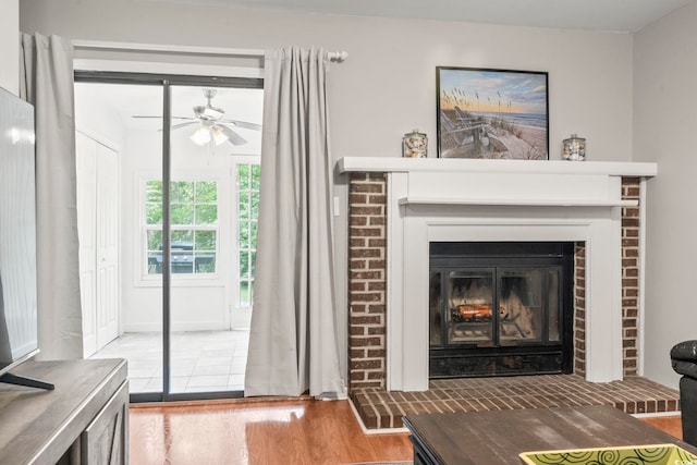 room details with wood finished floors, a ceiling fan, and a brick fireplace