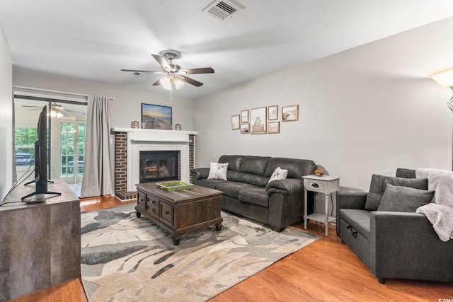 living room with visible vents, ceiling fan, light wood-type flooring, and a brick fireplace