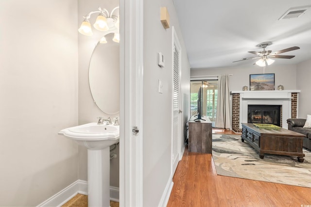 bathroom with wood finished floors, a fireplace, baseboards, visible vents, and a ceiling fan