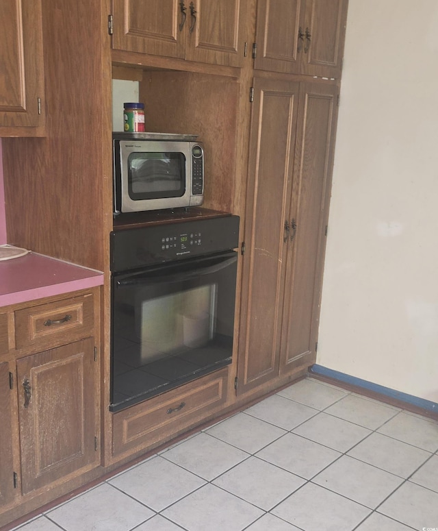kitchen with stainless steel microwave, brown cabinets, black oven, baseboards, and light tile patterned flooring