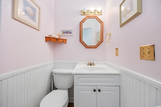 bathroom featuring vanity, toilet, a decorative wall, and a wainscoted wall