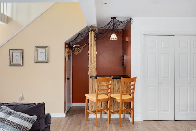 living area with baseboards, a bar, and light wood-type flooring