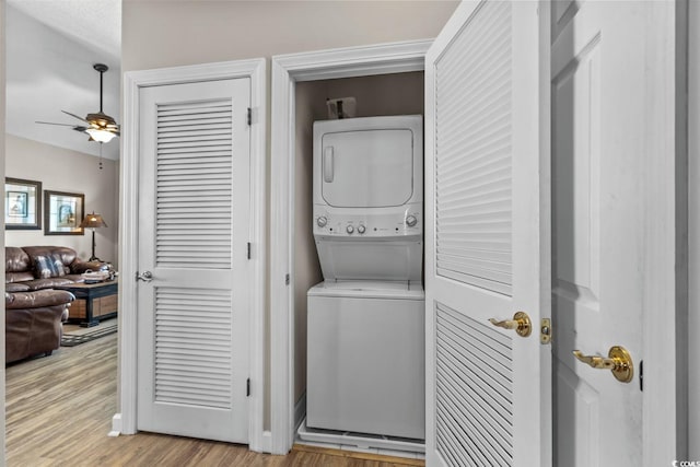 laundry area featuring laundry area, ceiling fan, light wood finished floors, stacked washing maching and dryer, and baseboards