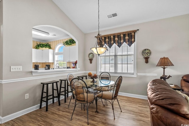 dining room featuring arched walkways, visible vents, wood finished floors, and lofted ceiling