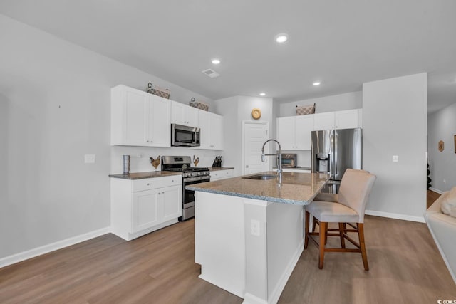 kitchen with white cabinets, a breakfast bar, stainless steel appliances, wood finished floors, and a center island with sink