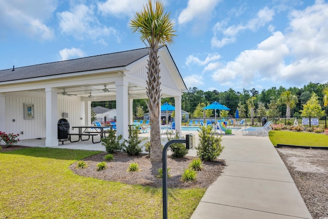 view of playground featuring fence, a patio, a community pool, a ceiling fan, and a lawn