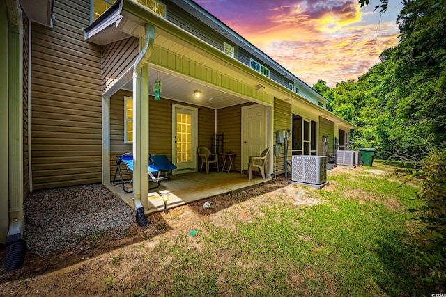 back of house at dusk featuring a patio, central AC unit, and a lawn