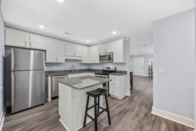 kitchen with appliances with stainless steel finishes, a center island, a sink, baseboards, and white cabinetry
