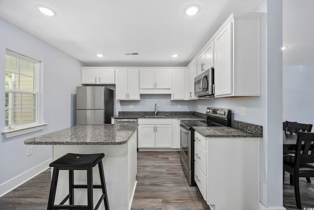kitchen with a kitchen island, a breakfast bar area, white cabinetry, a sink, and appliances with stainless steel finishes