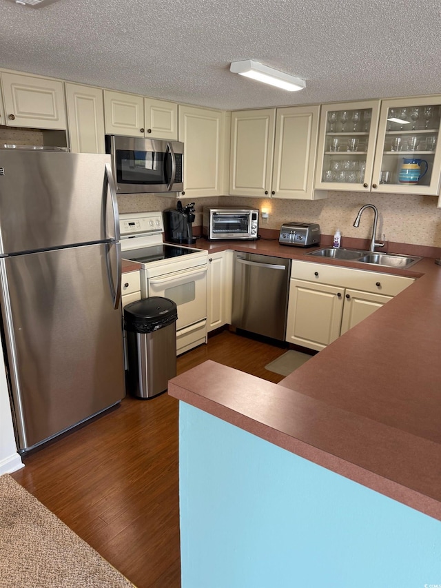 kitchen featuring appliances with stainless steel finishes, a sink, dark wood-style floors, glass insert cabinets, and a textured ceiling