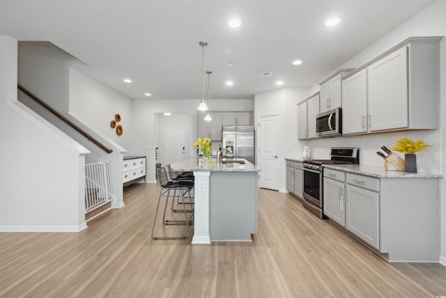 kitchen with light wood-style floors, appliances with stainless steel finishes, gray cabinetry, and a kitchen bar