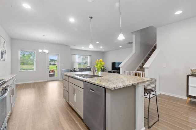 kitchen with a sink, dishwasher, light wood-style flooring, open floor plan, and a center island with sink