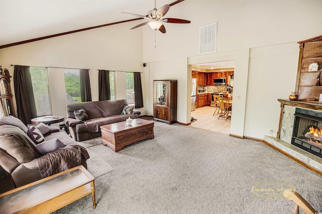 living room with light colored carpet, ceiling fan, visible vents, a lit fireplace, and high vaulted ceiling