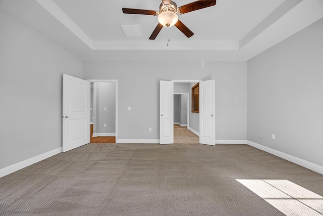 unfurnished bedroom featuring baseboards, a tray ceiling, a spacious closet, a ceiling fan, and carpet