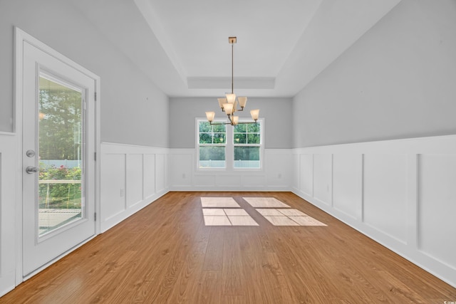 unfurnished dining area featuring wood finished floors, a decorative wall, a wainscoted wall, a tray ceiling, and a notable chandelier