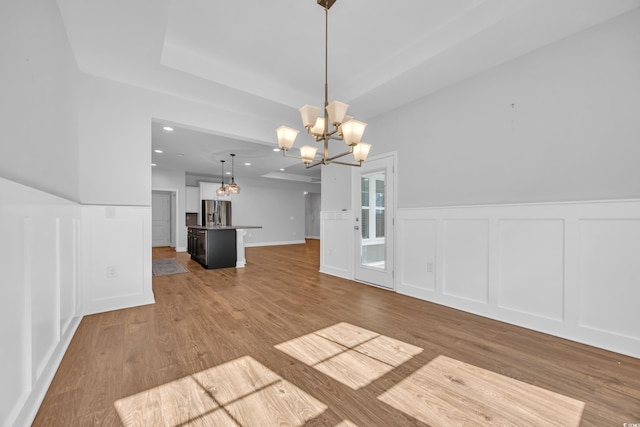 unfurnished dining area featuring an inviting chandelier, wainscoting, a decorative wall, recessed lighting, and wood finished floors