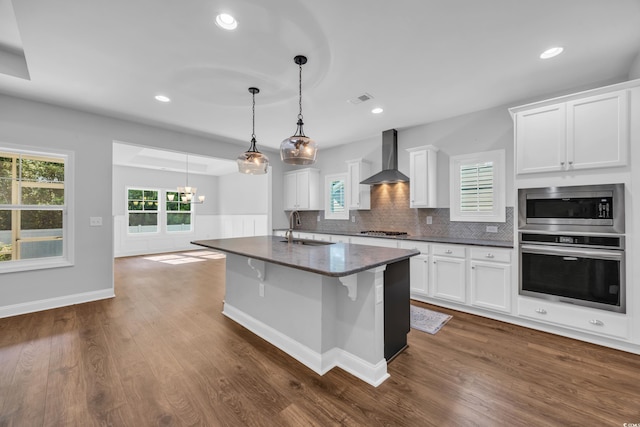 kitchen with wall chimney range hood, appliances with stainless steel finishes, a sink, white cabinetry, and visible vents