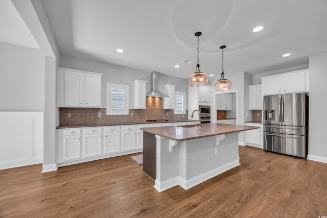 kitchen featuring appliances with stainless steel finishes, a sink, wall chimney exhaust hood, white cabinetry, and tasteful backsplash
